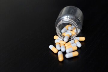 Pills on a dark wooden table, medication in capsules scattered from a bottle. Background for...