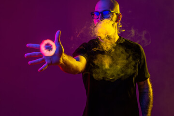 young man reaches for ring of smoke with his hand while blowing smoke. color filters. Vaping concept