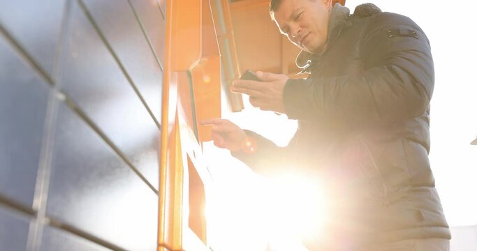 Man looking into mobile phone and dialing code on keypad of postal machine 4k movie