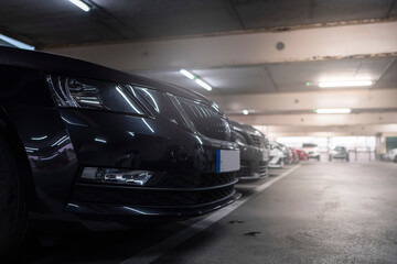Row of cars in a parking lot with dark color car in foreground. Selective focus. Light glow in the background. Nobody. Parking cost and vehicle density issue. Cinematic look