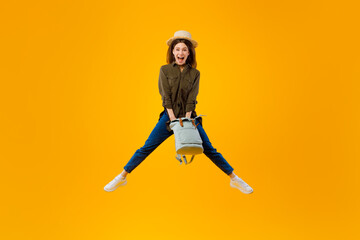 Excited Woman Holding Backpack Jumping In Mid Air, Yellow Background