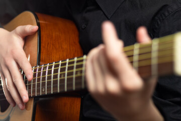 Obraz na płótnie Canvas The hands of a young musician playing an acoustic guitar with metal strings close-up with a blurred background. selective focus