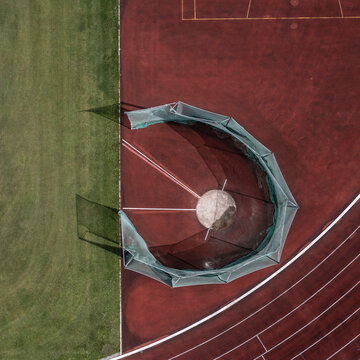 Aerial view fenced discus ring on red track in stadium infield
