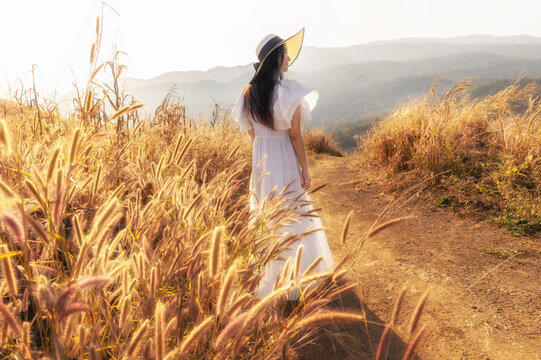 Beauty young girl outdoors enjoying nature. Asian woman in white dress walking on hillside meadow in summer mountains.