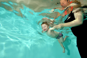 A laughing child with a disability with Down syndrome swims underwater in a children's pool with...