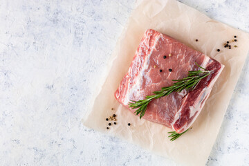 A piece of raw fresh pork with rosemary on a vax paper on white background. Meat with spices