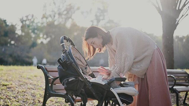 秋の公園・ベビーカーに乗った赤ちゃんをあやすお母さん	
