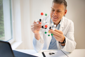 Chemist with blue shirt stands at height adjustable work table and works with model of molecules