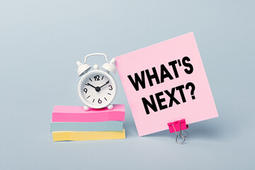 What's Next - concept of text on pink sticky note. Closeup of a personal agenda. Alarm clock and...