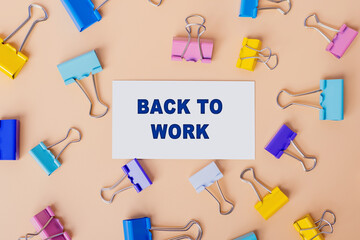 Back to work words written on white card. Top view image of business card and with many paper clips on beige background. Flat lay design