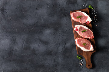 A pieces of raw fresh pork with rosemary on a cutting board on dark background. Meat with spices
