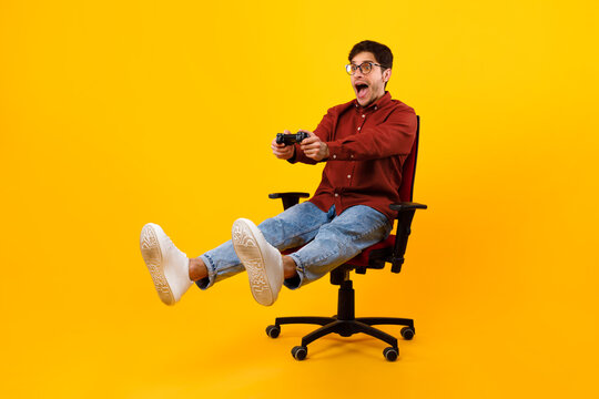 Male Gamer Shouting Playing Videogame Sitting In Chair, Yellow Background