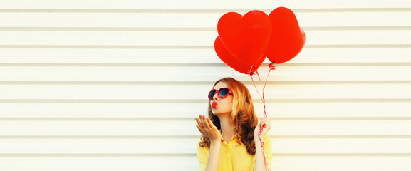 Portrait of beautiful young woman with red heart shaped balloon blowing her lips sending sweet air...