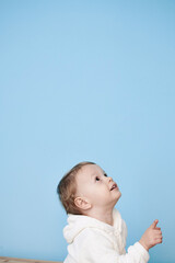 a little boy of 2 years sits in a white jacket on a blue background and thinks laughs happy sad sadness cheerful advertisement for children