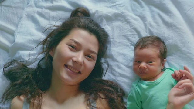 Mother and baby son making selfie or video call to father, Asian family at home, young woman and boy use smartphone, togetherness, childhood and motherhood lifestyle, pretty kid and mom in bedroom