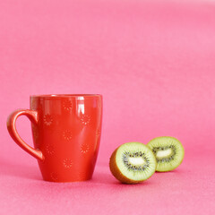 a red mug on a pink background and a ripe kiwi in the cut