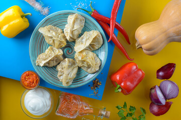 top view of a turquoise plate with manti on a yellow and blue background with spices
