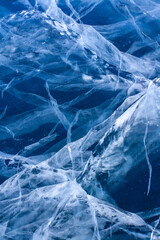 Natural texture of clear blue ice with white cracks. Thick ice and deep cracks. Vertical.