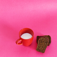 red cup with milk and black bread on a pink background