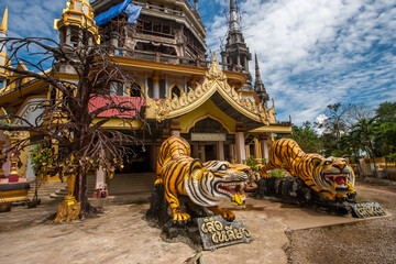Two sculptures of tigers and a wish tree at the entrance to a Buddhist temple. Tigers are yellow with black stripes.