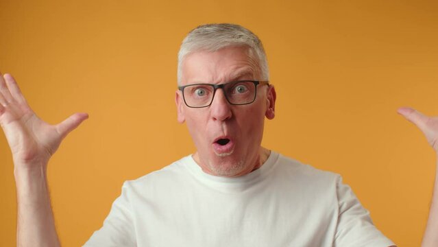 Senior man with exploding head gesture against yellow background