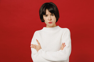 Fototapeta premium Young disappointed annoyed sad unhappy woman 20s wearing white knitted sweater look camera hold hands crossed folded isolated on plain red color background studio portrait. People lifestyle concept.