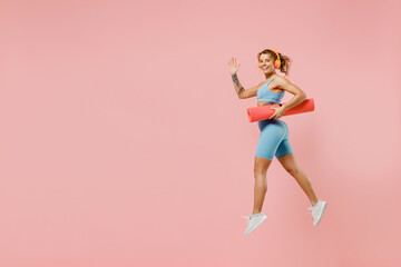Fototapeta na wymiar Full body young strong sporty fitness trainer instructor woman wear blue tracksuit headphones spend time in home gym hold caremat isolated on pastel plain light pink background. Workout sport concept.