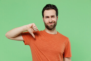 Young displeased disappointed sad man 20s wear casual orange t-shirt showing thumb down dislike...