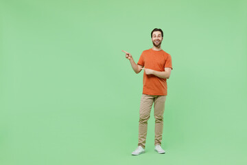 Full body young man 20s wear casual orange t-shirt point index finger aside on workspace area mock up isolated on plain pastel light green color background studio portrait. People lifestyle concept.