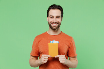 Traveler smiling tourist man wear orange t-shirt hold passport tickets isolated on pastel plain...