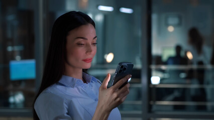 Side view of successful businesswoman use mobile phone standing near window in office