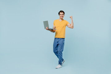 Full body excited young man 20s wear yellow t-shirt hold use work on laptop pc computer do winner...