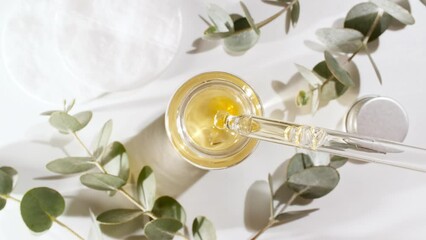 Oil drips from pipette into bottle. Eucalyptus extract, aromatic, essential oil. Cosmetics oils based on natural ingredients. Natural cosmetics production for hair and skin care. Top view. 4k 