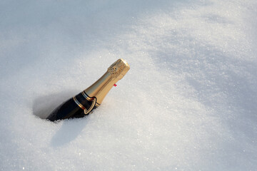 Bottle of champagne with gold foil buried in snow
