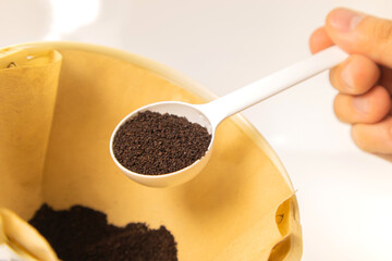 Putting grinded dark roast coffee in a natural unbleached coffee filter with a coffee measuring scoop. 