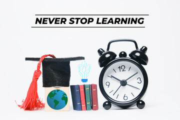 A picture of earth at wooden block wearing mortarboard, book and alarm clock miniature with never stop learning word.