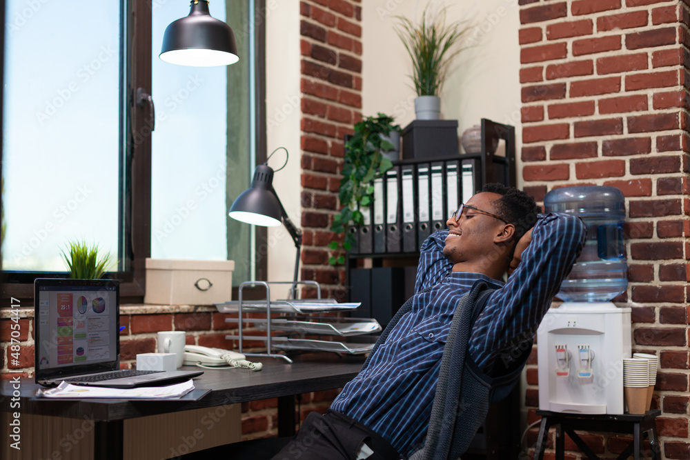 Poster smiling startup owner stretching on chair taking a break sitting at desk in front of laptop with bus