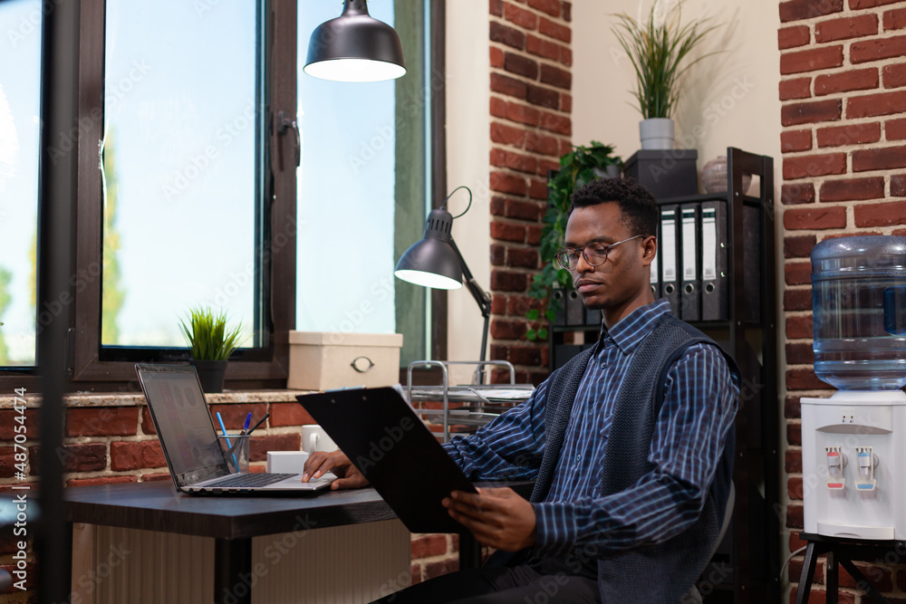 Poster startup employee holding clipboard with bussiness charts sitting at desk comparing data with sales r