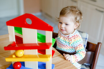 Little baby girl playing with educational toys at home or nursery. Happy healthy toddler child having fun with colorful wooden toy ball track. Kid learning to hold and roll balls. Motoric education.