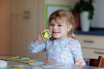 Excited smiling cute toddler girl playing picture card game. Happy healthy child training memory,...