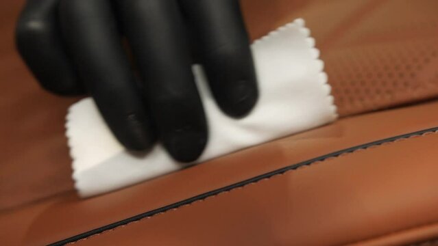 Detailing wax leather seat brown. Cleaning the seat surface with a white sponge held by a worker's hand in a black glove.
