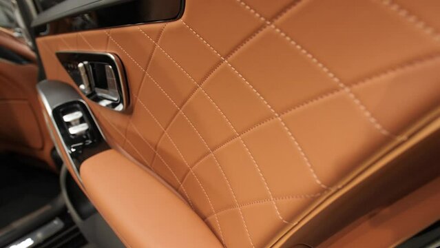 Brown leather surface of the front door of the interior of a prestigious, expensive, new car.