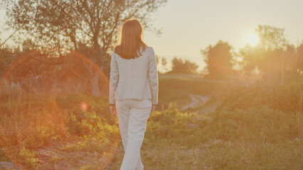 Beautiful girl walks in the countryside in front of the setting sun