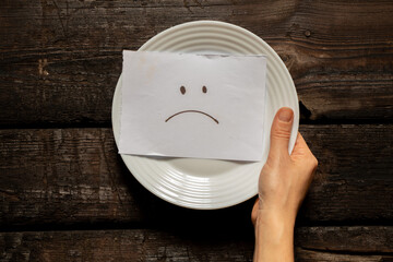 a sad emoticon is drawn on a card that lies on a white plate in the hands of a girl on the table, a...