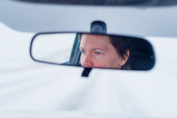 Face of a female driver in car rear-view mirror while driving in bad conditions during snow blizzard