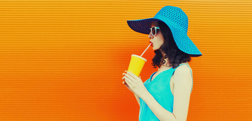 Portrait of beautiful young woman drinking fresh juice from cup wearing summer hat on orange...