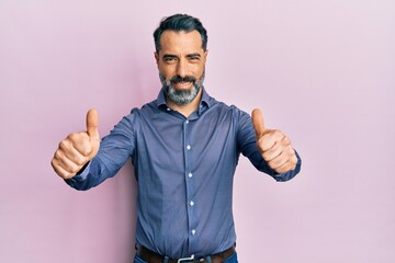 Middle age man with beard and grey hair wearing business clothes approving doing positive gesture with hand, thumbs up smiling and happy for success. winner gesture.