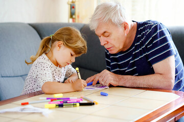 Cute little preschool girl and handsome senior grandfather painting with colorful felt pens and...