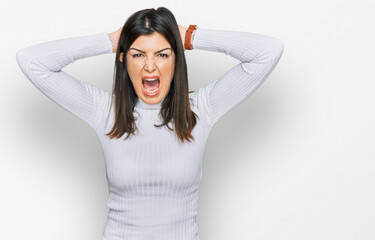 Beautiful brunette woman wearing casual clothes crazy and scared with hands on head, afraid and...
