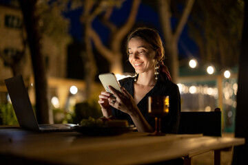 Caucasian woman watching something on laptop and phone at evening time outdoors. Young woman...